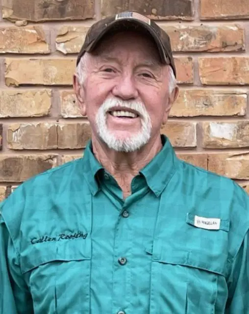 A man in a green shirt and hat standing next to a brick wall.